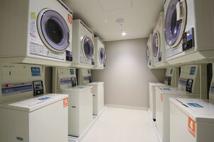 A laundry facility with multiple washing machines and dryers, each with control panels and labels.