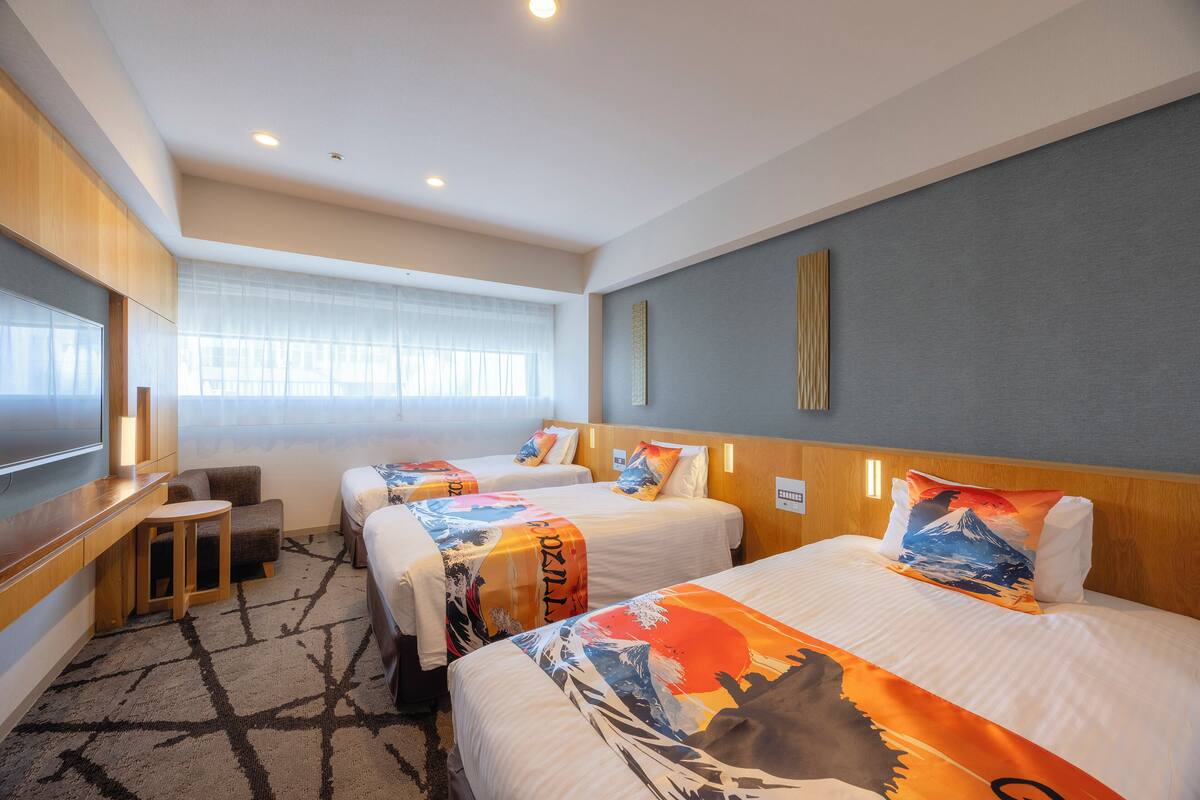 A hotel room with two beds, a desk, and a TV.