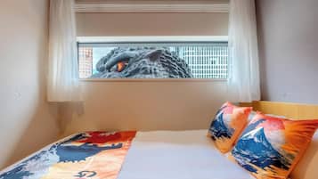 Una cama con una colcha y almohadas coloridas, una ventana con vistas a un paisaje urbano y cortinas de encaje.
