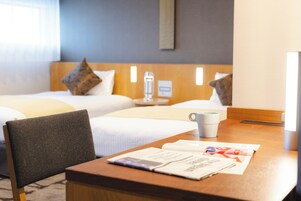 Een hotelkamer met twee bedden, een houten tafel, een stoel, een lamp en een tijdschrift.