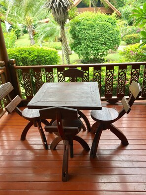 A wooden deck with a table and chairs, surrounded by a decorative railing and lush greenery in the background. - Baan Laem Noi Villa (Koh Samui)
