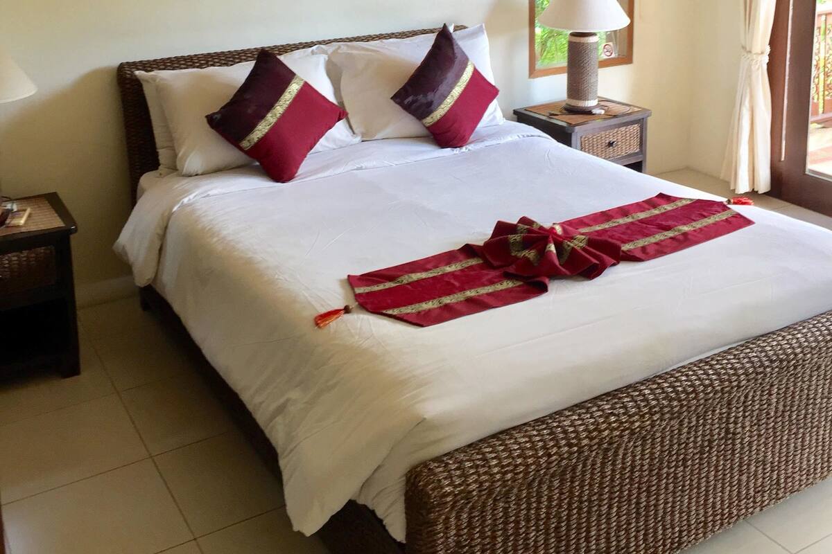 Una habitación de hotel con una cama grande, una mesita de noche, una lámpara y una ventana con cortinas.