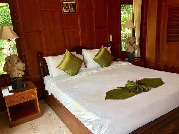 A neatly made bed with white linens and green pillows, a wooden nightstand with a lamp, and a small statue beside the bed. - Baan Laem Noi Villa (Koh Samui)