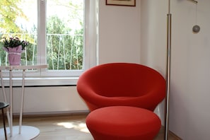 A red chair and a small table with a potted plant in a room with a window and a white wall. - GoVienna Charming Studio (Vienna)