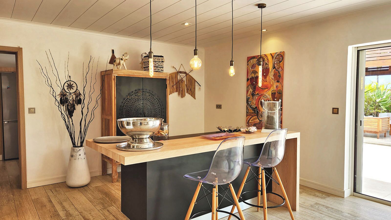 Una cocina moderna con una isla de madera, sillas transparentes e iluminación colgante.