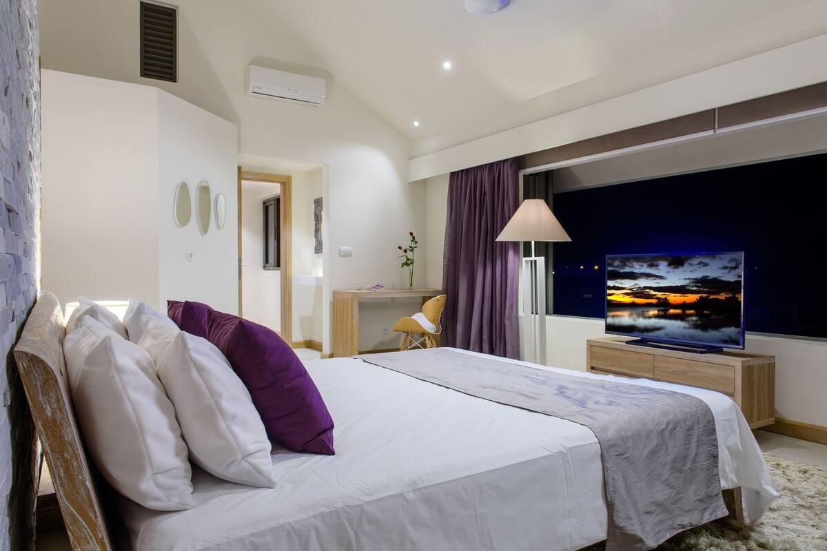 Ein modernes Schlafzimmer mit Bett, Schreibtisch und Fernseher, der eine Sonnenuntergangsszene zeigt.