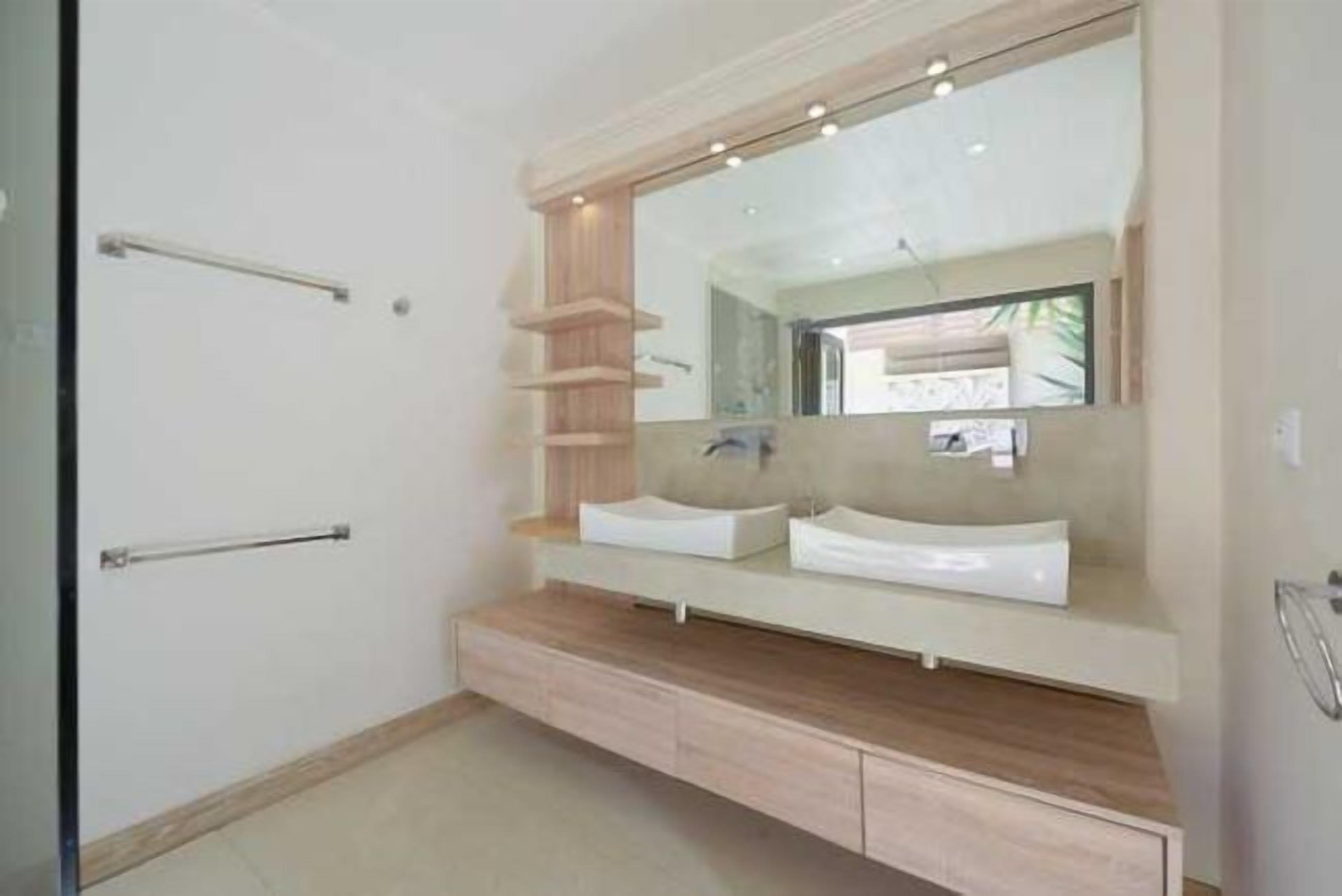 A modern bathroom with a large mirror, two sinks, wooden shelves, and a towel rack.