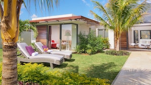 A modern house with a glass facade, a well-maintained lawn, and two lounge chairs with cushions. - Clos du Littoral by Fine and Country (Grand-Baie)