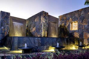 A stone wall with a water feature and a logo. - Clos du Littoral by Fine and Country (Grand-Baie)