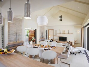 A spacious dining area with a wooden table, white chairs, and hanging pendant lights. - Clos du Littoral by Fine and Country (Grand-Baie)