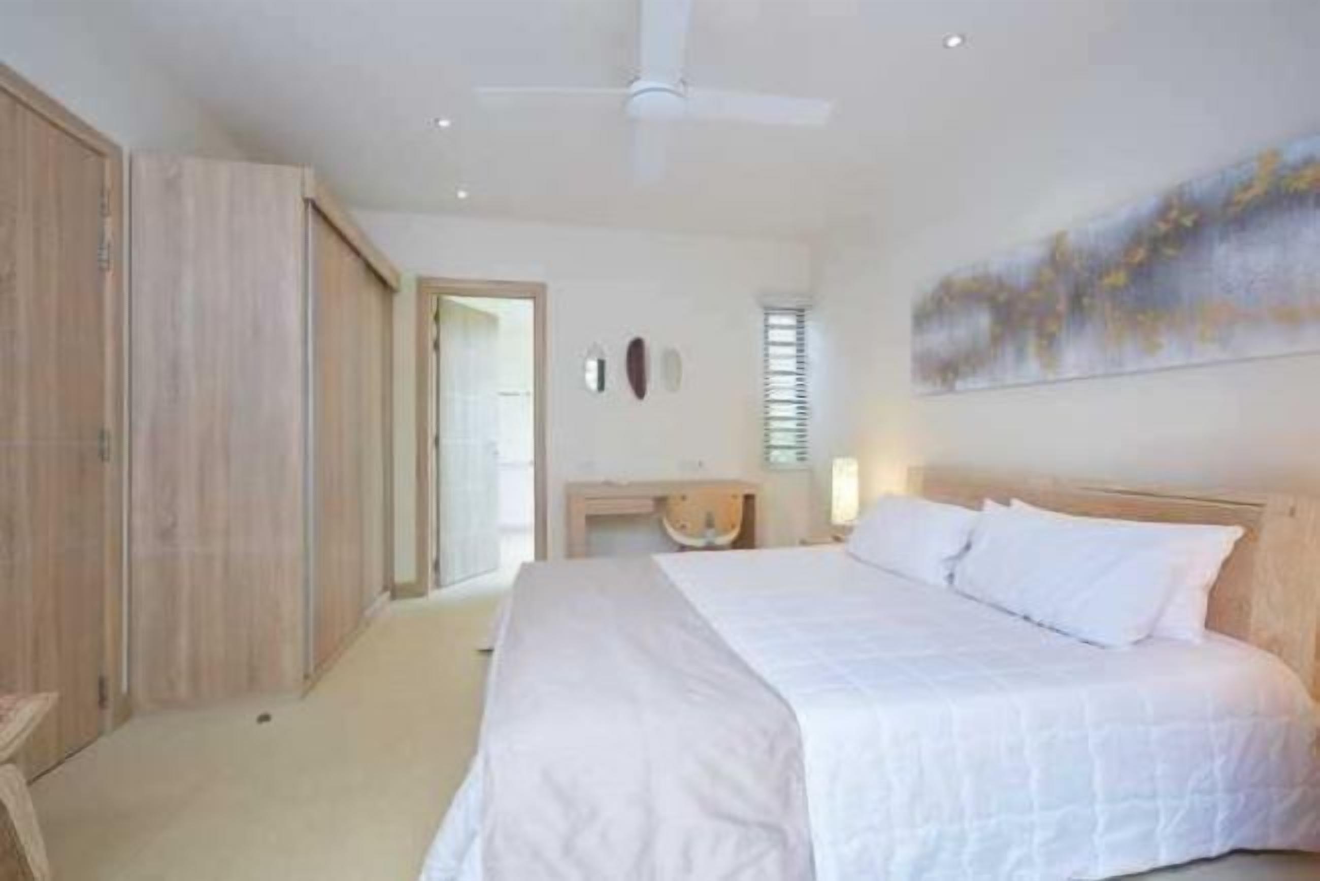A bedroom with a bed, a nightstand, a ceiling fan, and a door leading to another room.