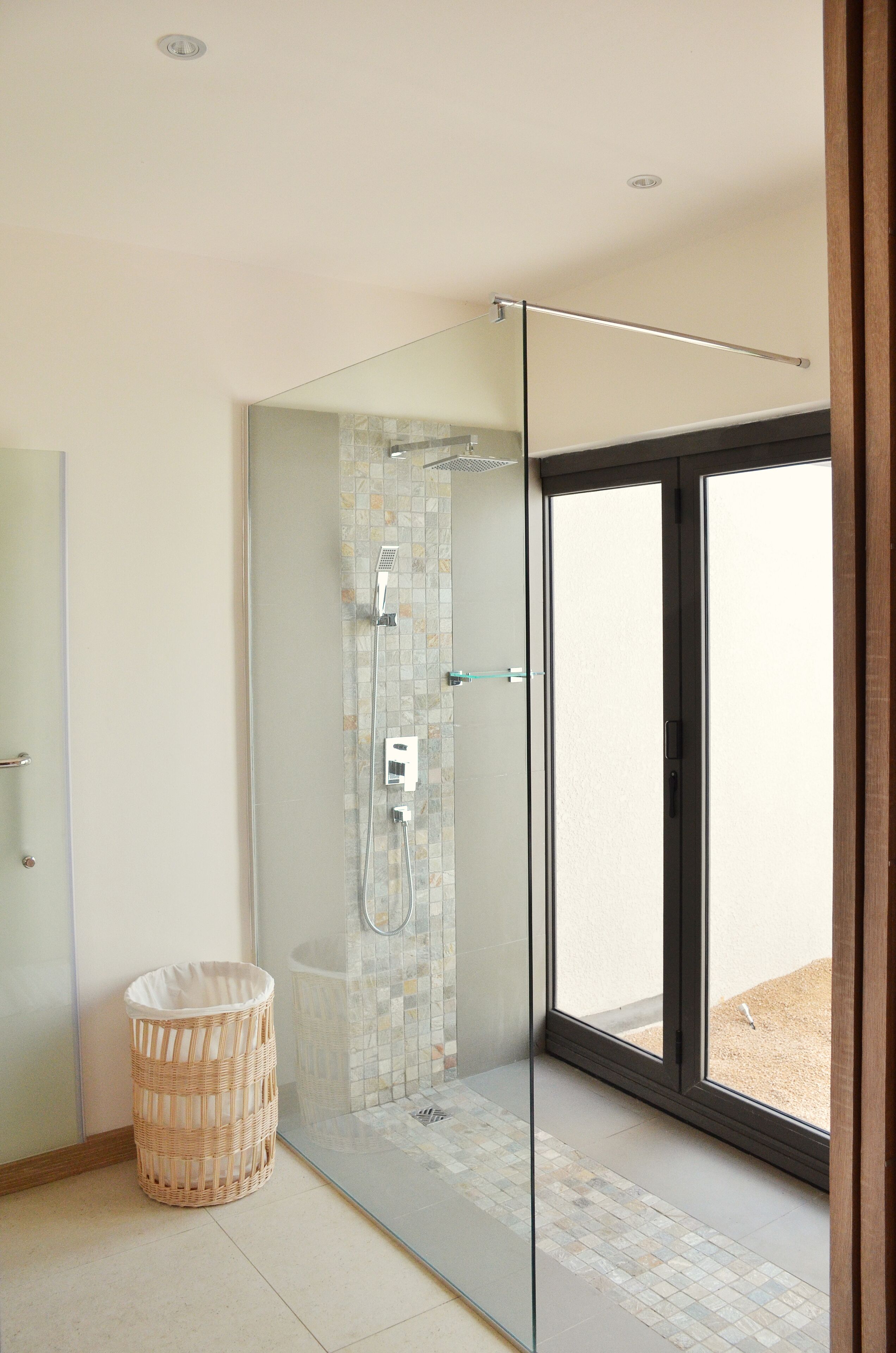 A modern bathroom with a glass shower enclosure, a wicker basket, and a view through the glass door.