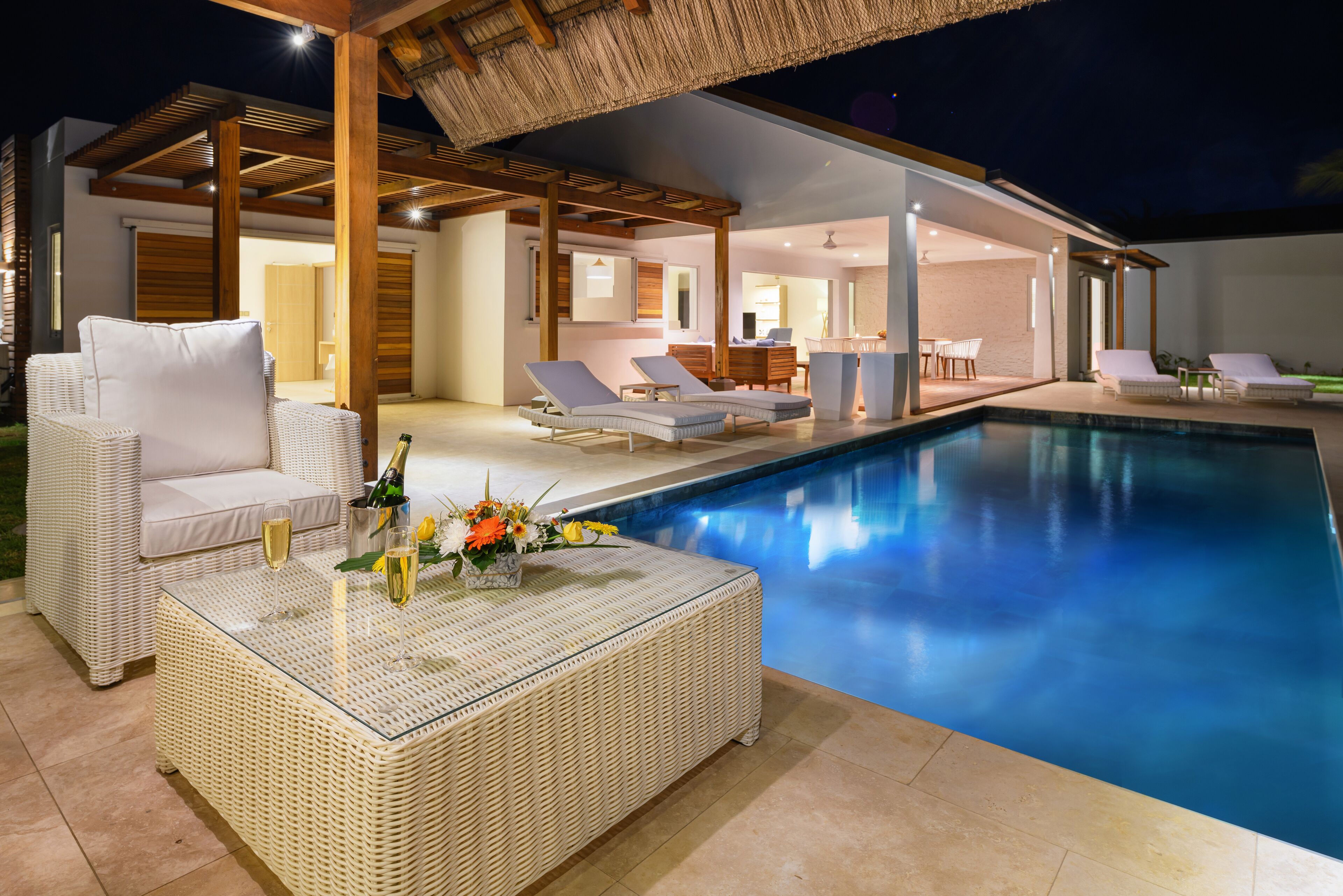 A modern outdoor pool area with lounge chairs and a wicker table with drinks.