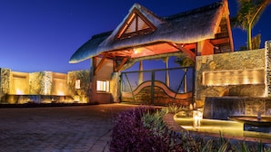 A thatched-roof building with a stone facade, a gated entrance, and a sign reading "CLOS DU LITTORAL GRAND BAILE". - Clos du Littoral by Fine and Country (Grand-Baie)