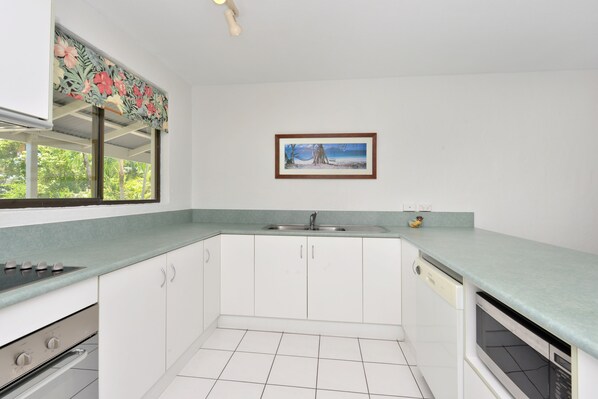 A kitchen with white cabinets, a green countertop, a sink, and a window with a floral curtain.