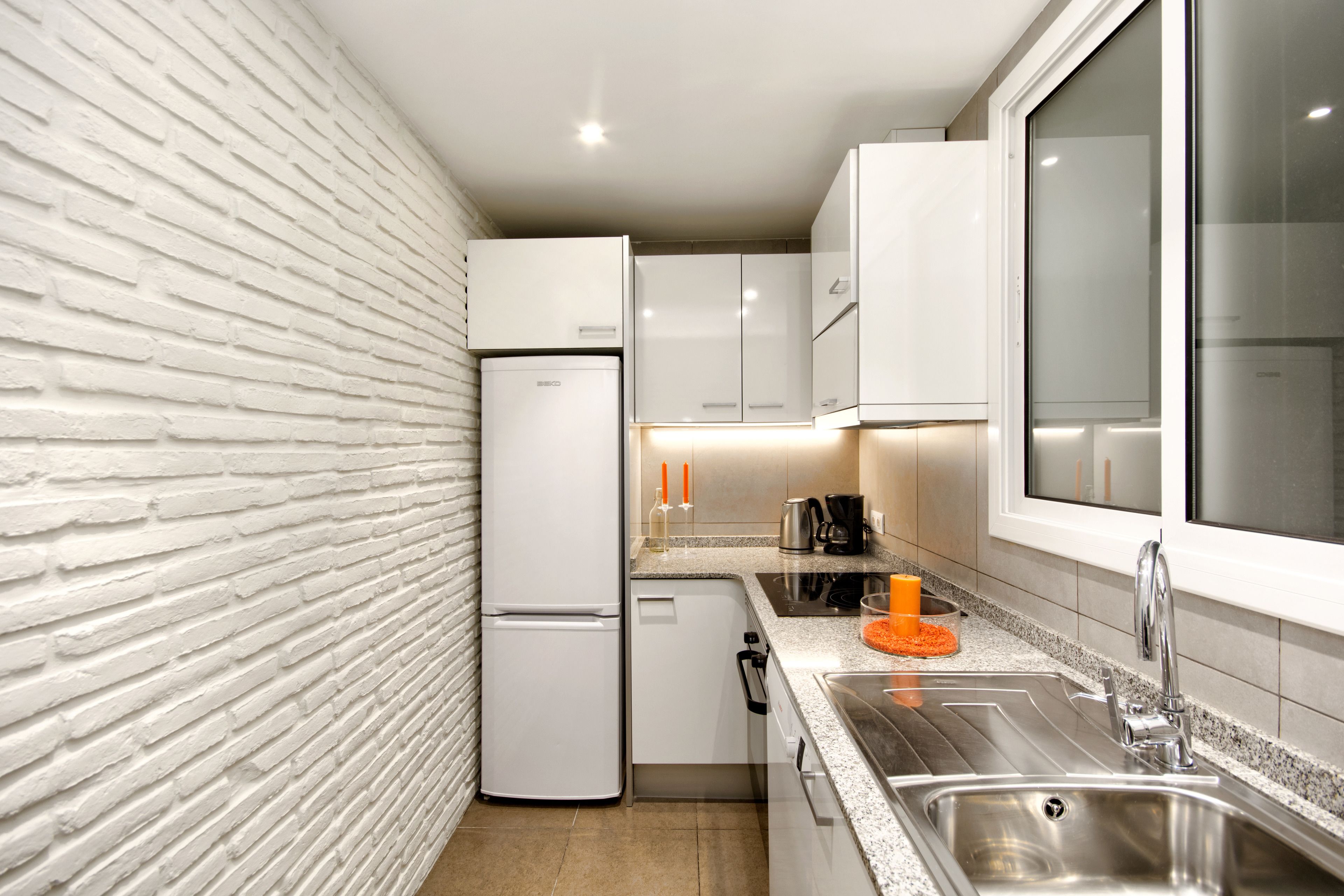 A compact kitchen with white appliances, a granite countertop, and a window with frosted glass.