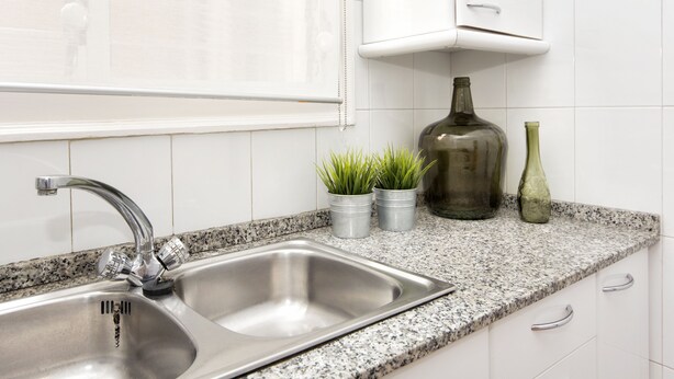 Una cocina con pileta de acero inoxidable, encimera de granito y muebles bajos blancos.