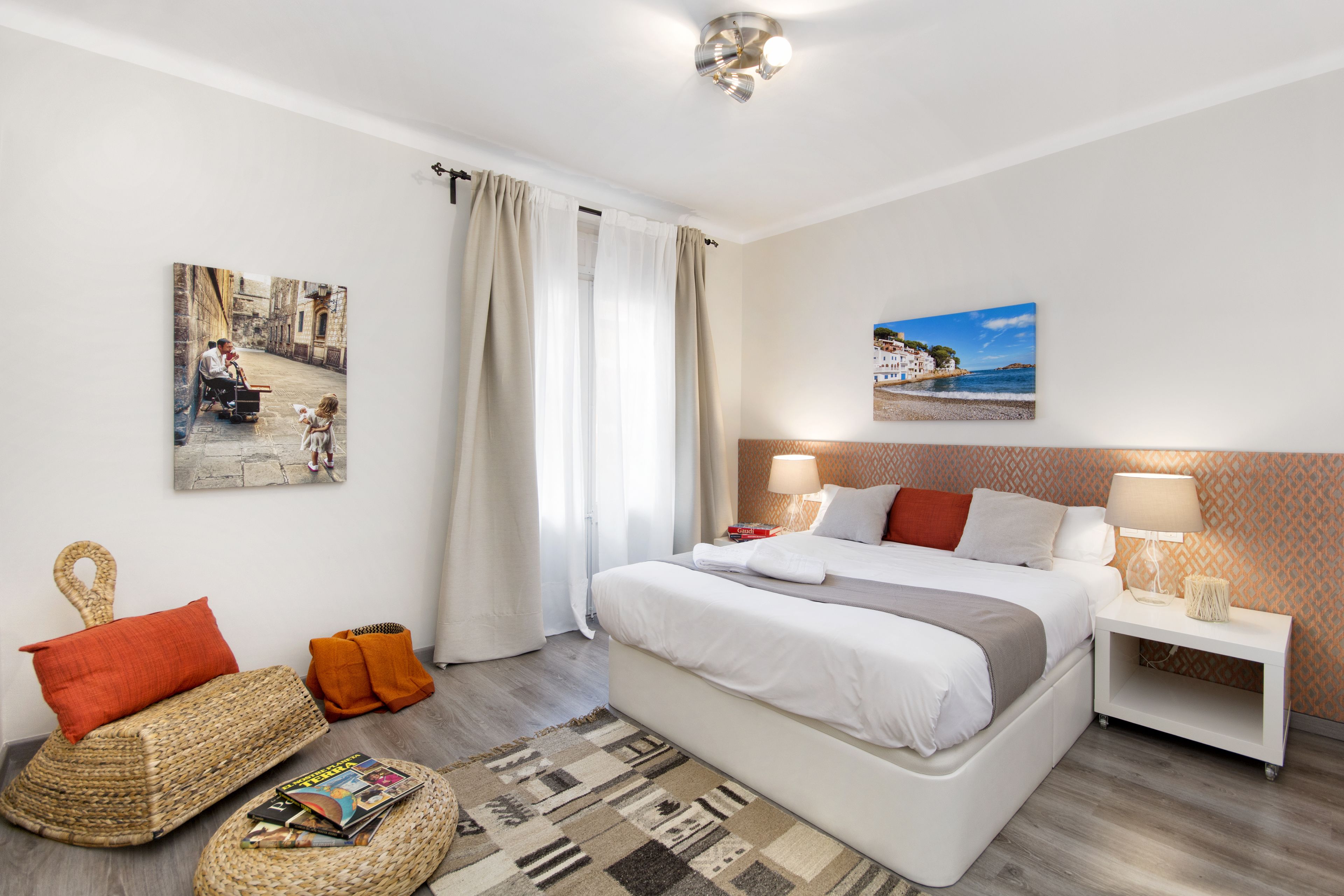 A modern hotel room with a large bed, a bedside table with a lamp, a wall-mounted painting, and a view of the sea.