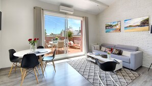 Una sala de estar moderna con un sofá gris, una mesa de comedor con sillas y un amplio ventanal corredero que da a un patio exterior.