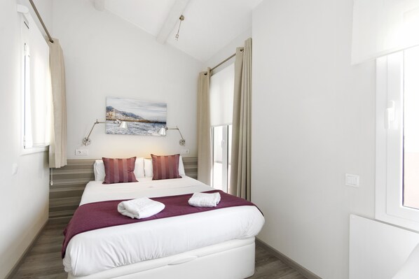 Ein Hotelzimmer mit einem großen Bett, einem Fenster mit Vorhängen, einem Gemälde an der Wand und einer Nachttischlampe.