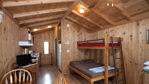 A wooden cabin interior with a bunk bed, a desk with a computer, a chair, and a small kitchenette. - Medina Lake RV Campground (Pipe Creek)