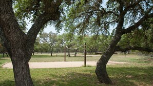 A park with large trees, a swing set, and a dirt path. - Medina Lake RV Campground (Pipe Creek)
