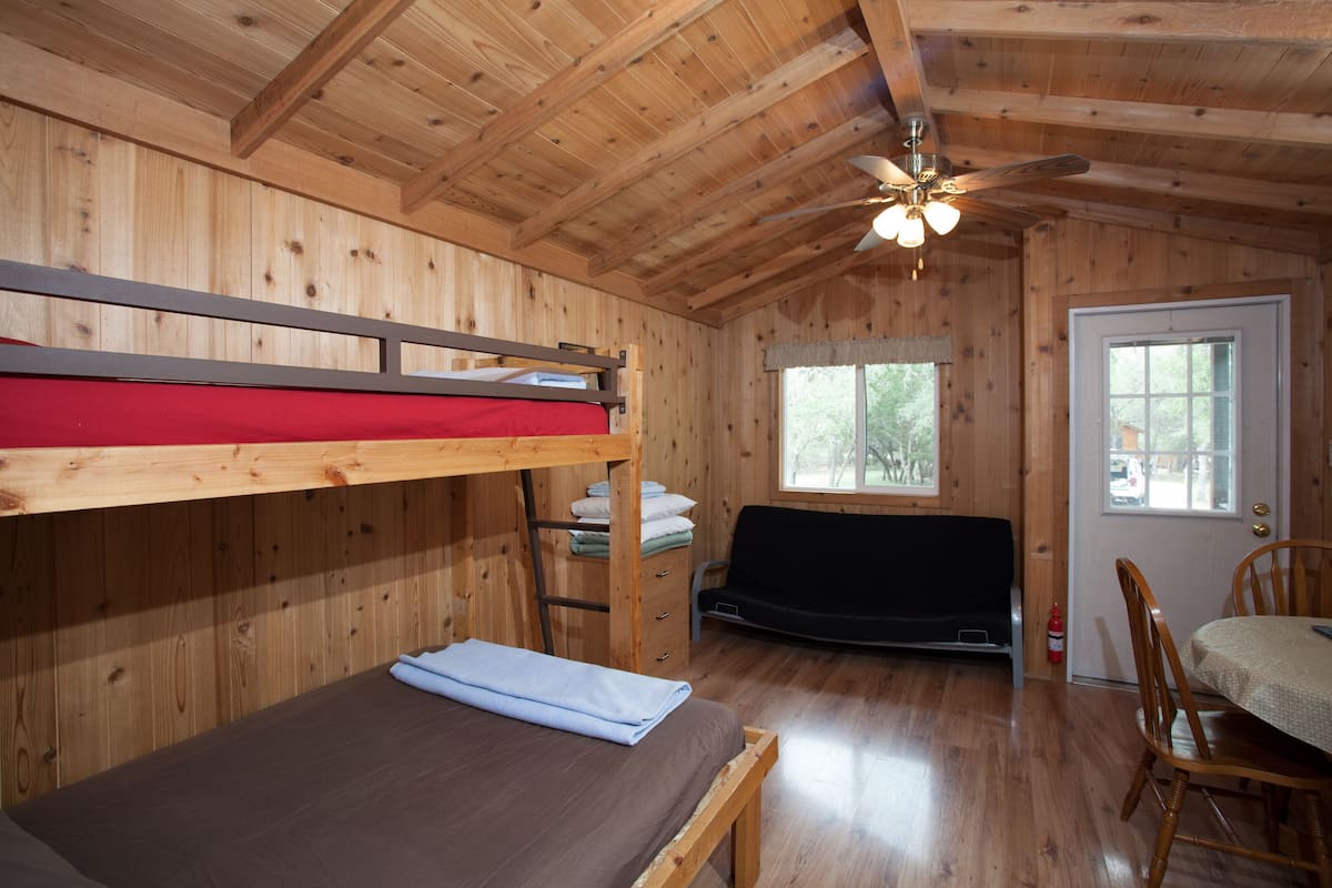 A wooden cabin with a bunk bed, a dining table with chairs, and a ceiling fan.
