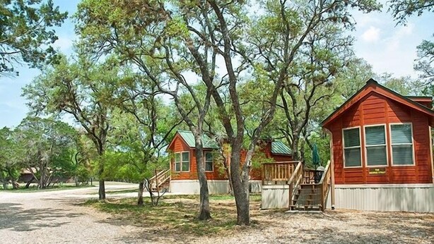 A cabin with a wooden deck and a staircase leading to the entrance. - Medina Lake RV Campground (Pipe Creek)