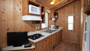 A compact kitchen with wooden walls, a stove, a microwave, a sink, and a refrigerator. - Medina Lake RV Campground (Pipe Creek)