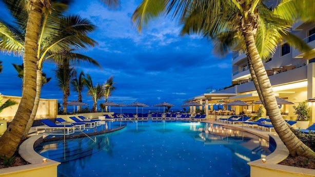A swimming pool with lounge chairs and palm trees, surrounded by a building with multiple floors.