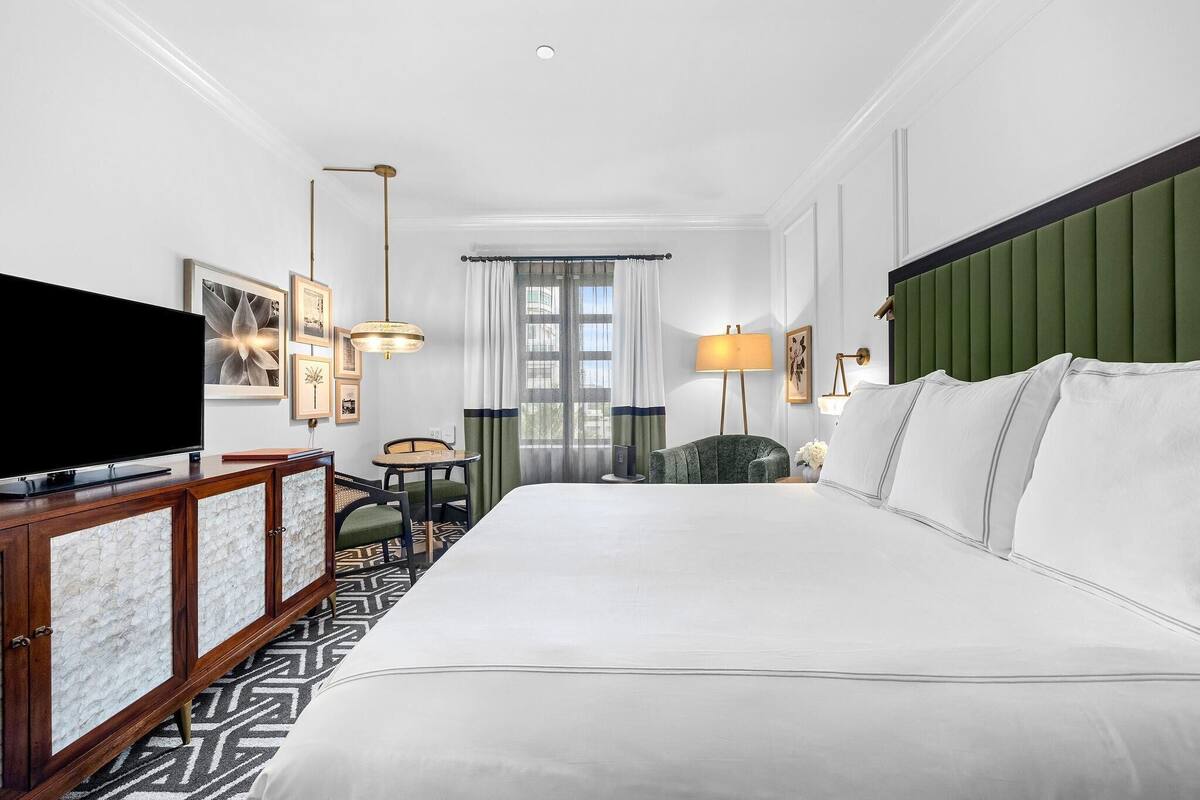 A hotel room with a large bed, a TV, a wooden cabinet, a desk, and a chair.