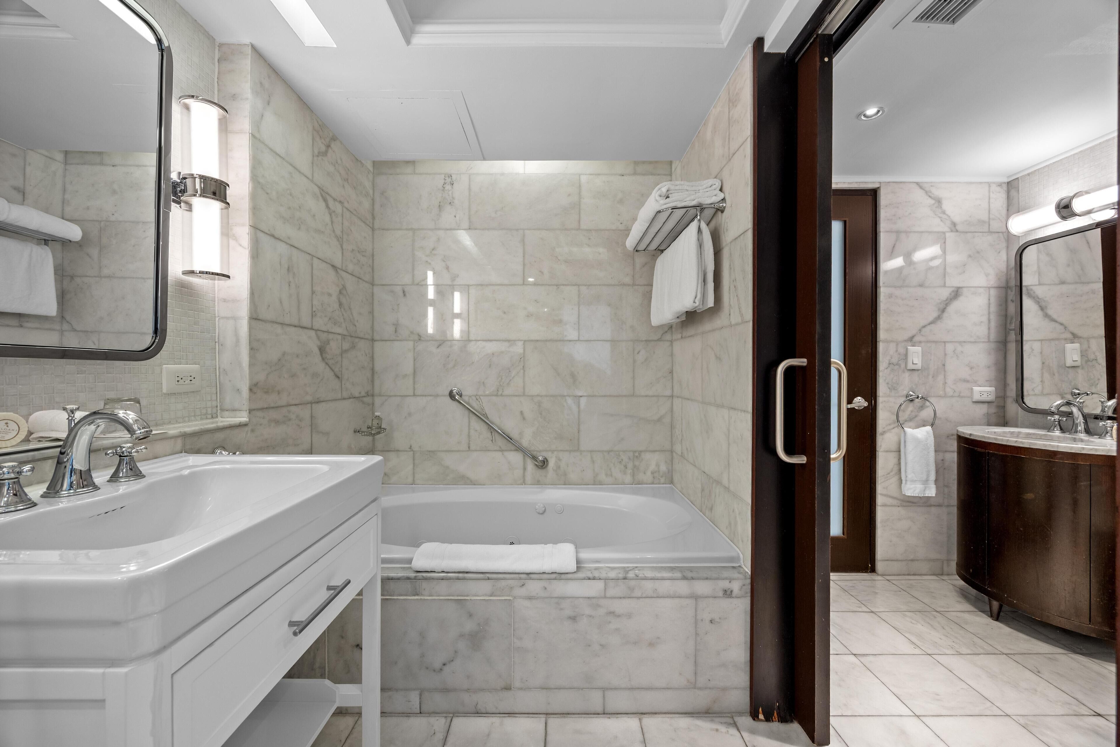 A modern bathroom with a double sink, a bathtub, and a large mirror.
