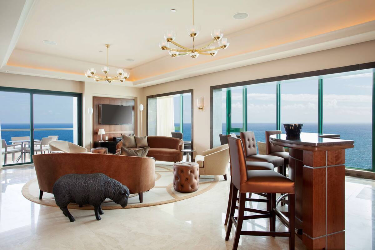 A spacious living room with a large view of the ocean, a plush sofa, a coffee table, and a bar area.