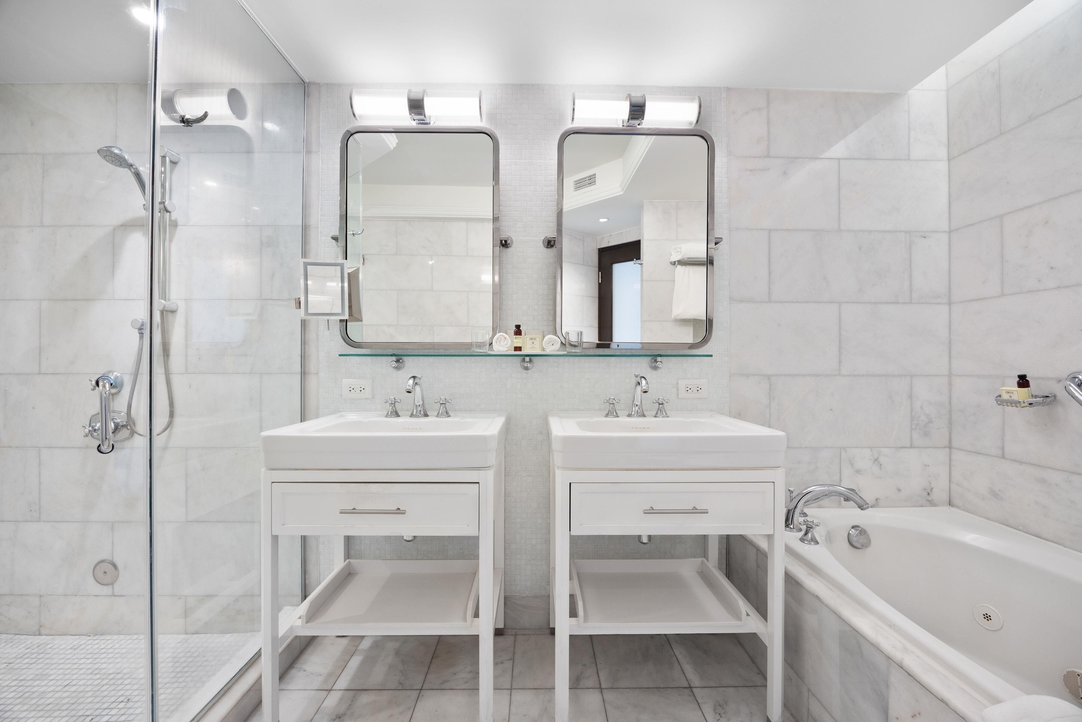 A modern bathroom with two sinks, a glass shower enclosure, and a bathtub.