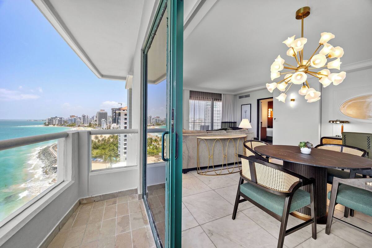 A balcony with a city view, a dining area with a round table and chairs, and a modern chandelier.