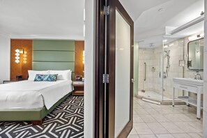 A hotel room with a bed, bedside table, and a nightstand. There is a bathroom with a shower, sink, and mirror. - Condado Vanderbilt Hotel (San Juan)
