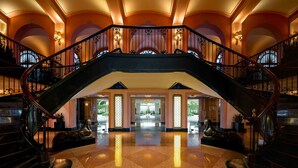 A grand lobby with a central staircase, polished floors, and decorative lighting.