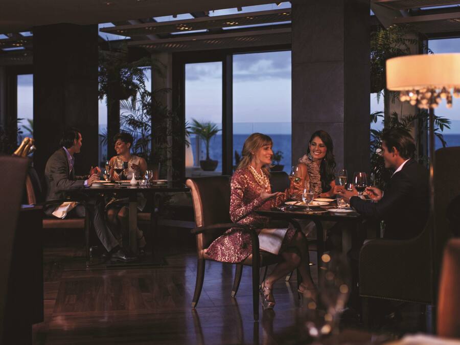 Een restaurant met uitzicht op de oceaan, grote ramen en een kroonluchter.