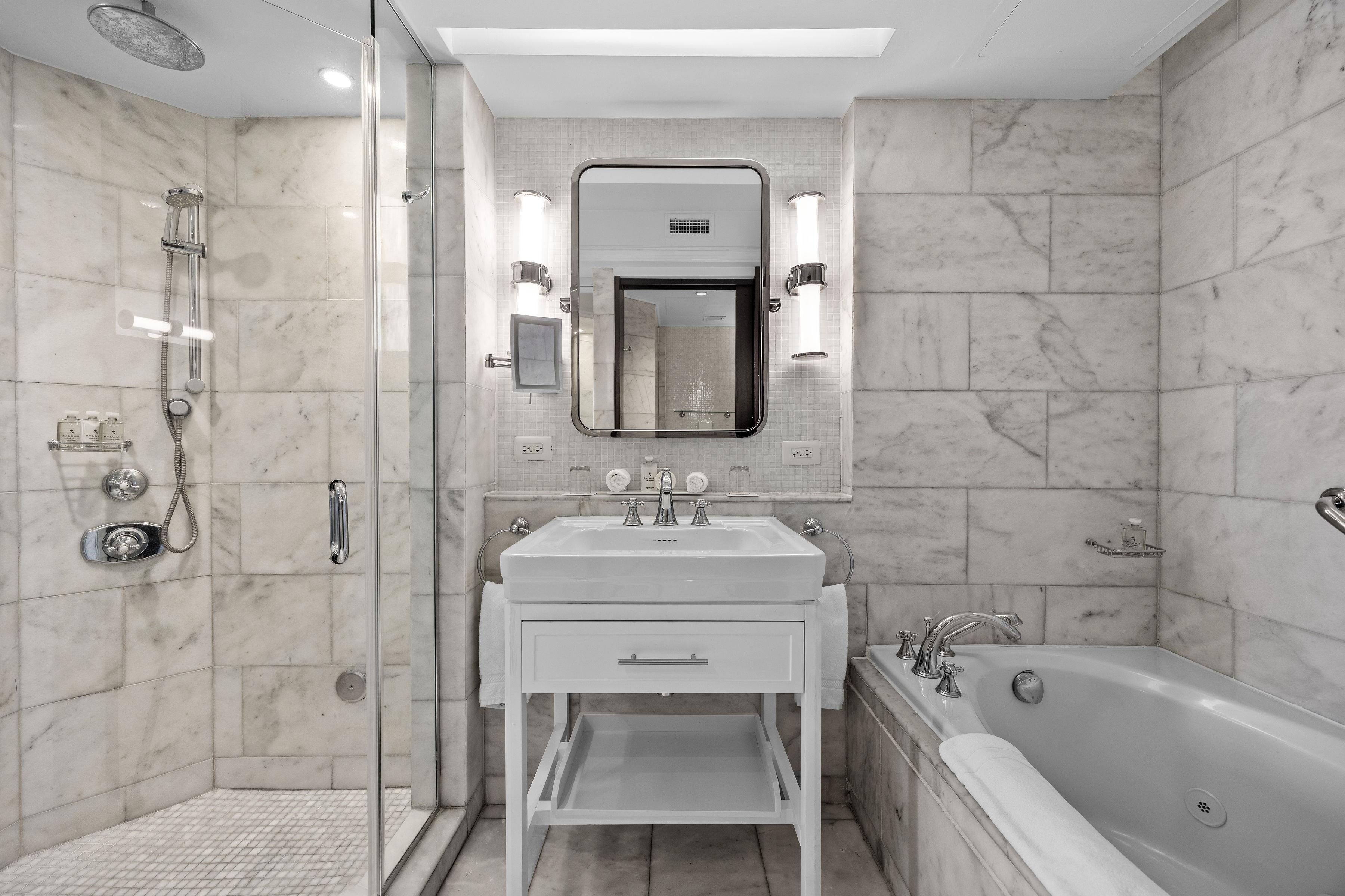 Un baño moderno con ducha de vidrio, tocador blanco con espejo y bañera independiente.