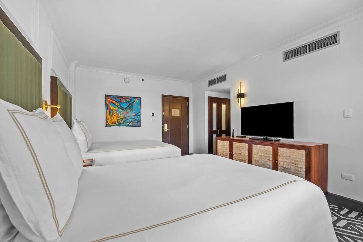 A hotel room with two beds, a flat-screen TV, a painting, and a wooden cabinet.