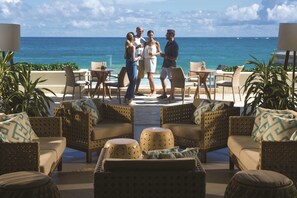 A terrace with wicker furniture, a view of the ocean, and a group of people conversing. - Condado Vanderbilt Hotel (San Juan)