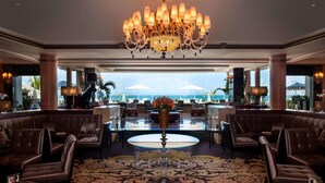 A spacious lobby with a large chandelier, leather seating, a central table, and a view of the ocean.
