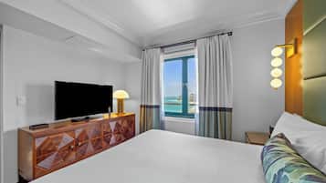 A hotel room with a large bed, a TV on a wooden cabinet, a nightstand, and a view of the ocean.