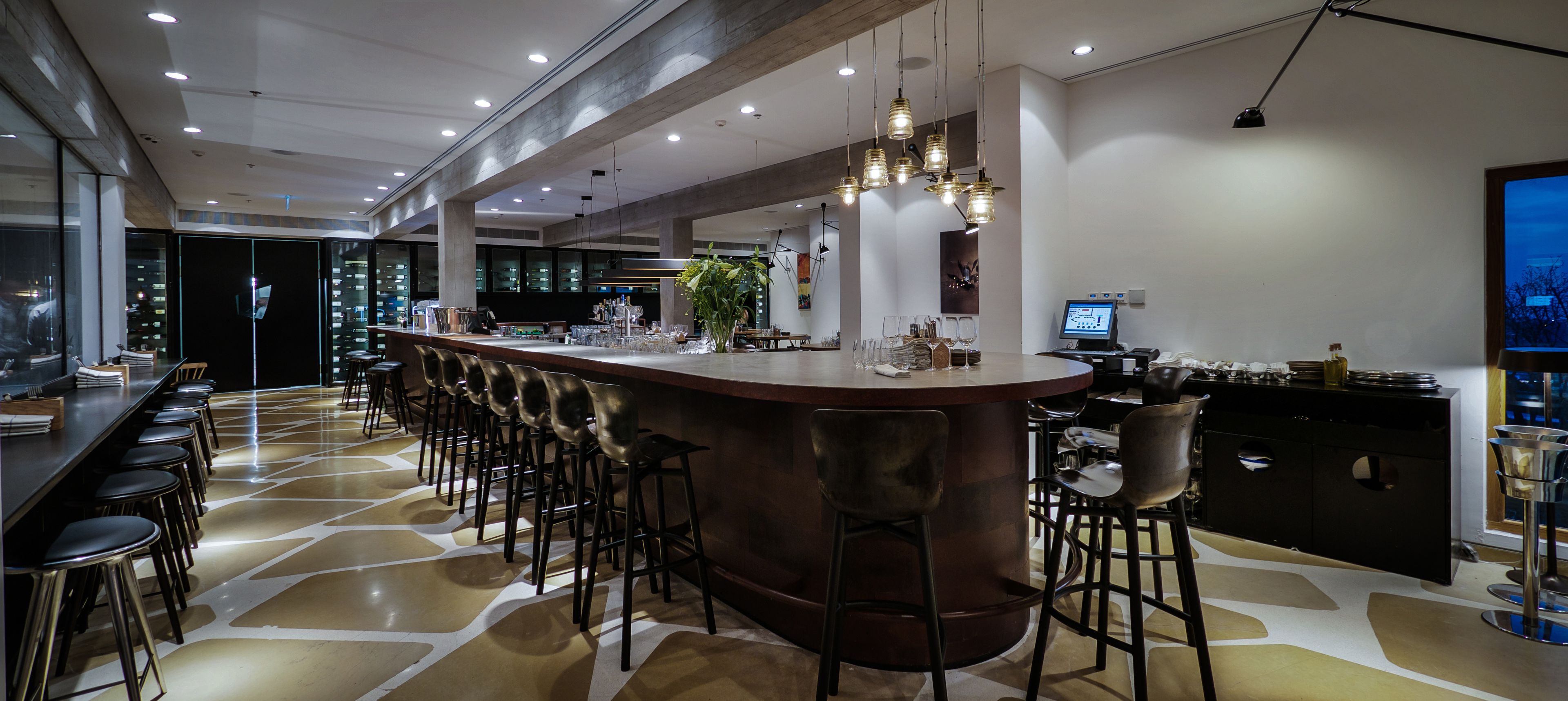 Un espace bar moderne avec un long comptoir, de nombreux tabourets et une grande plante en pot.