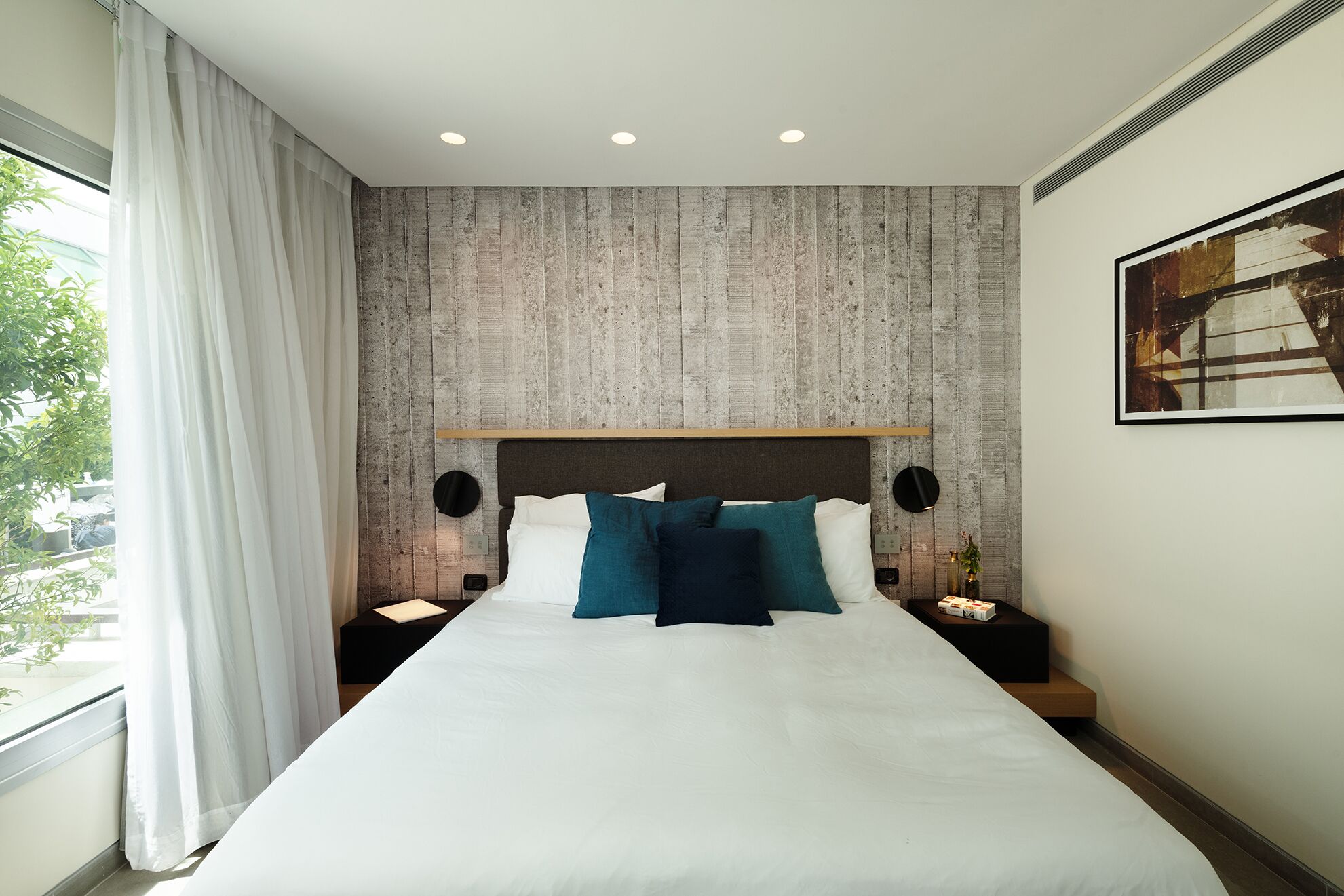 A modern hotel room with a large bed, a wooden accent wall, and a painting on the wall.