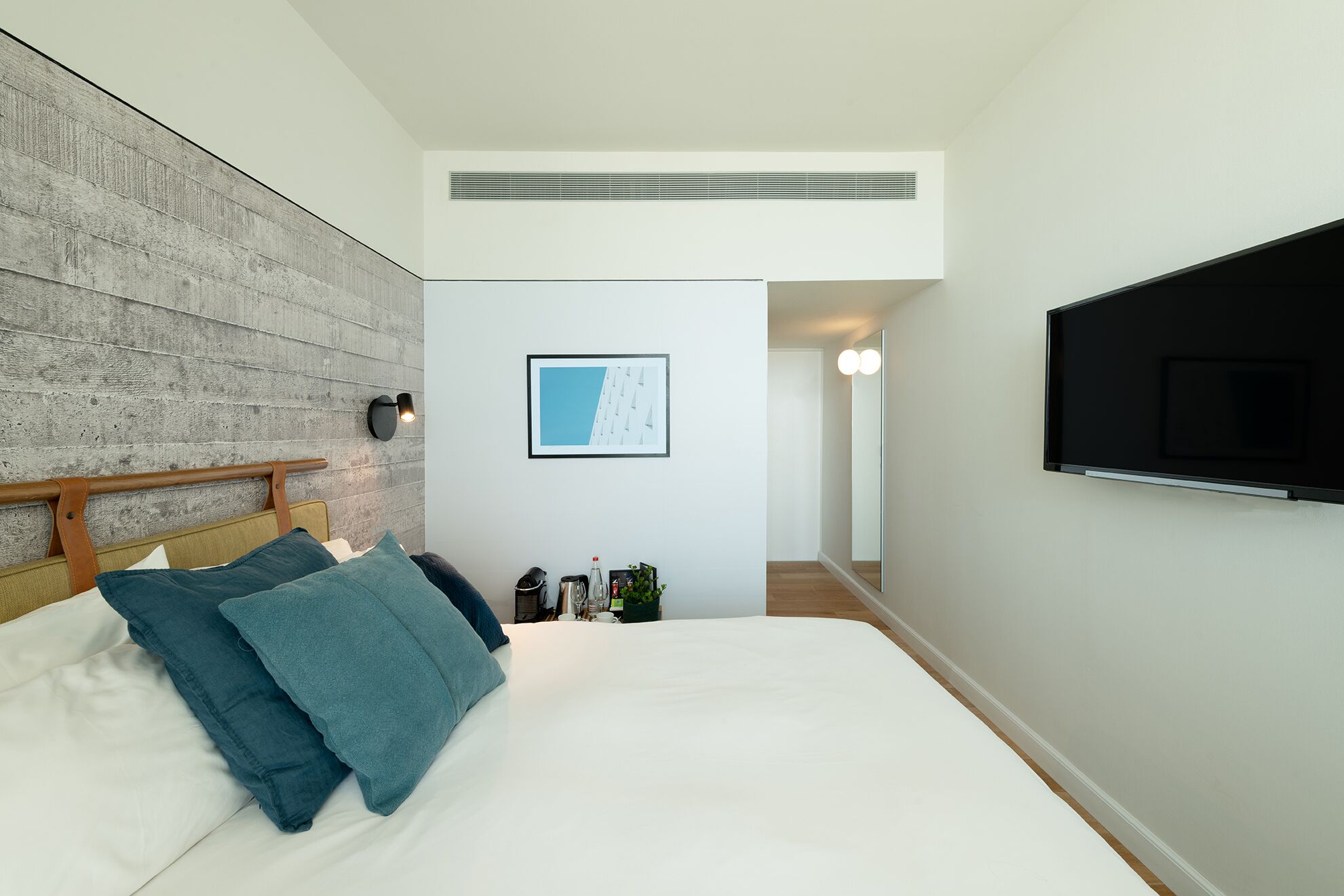 A modern bedroom with a large bed, a mounted TV, a framed picture on the wall, and a wooden headboard.
