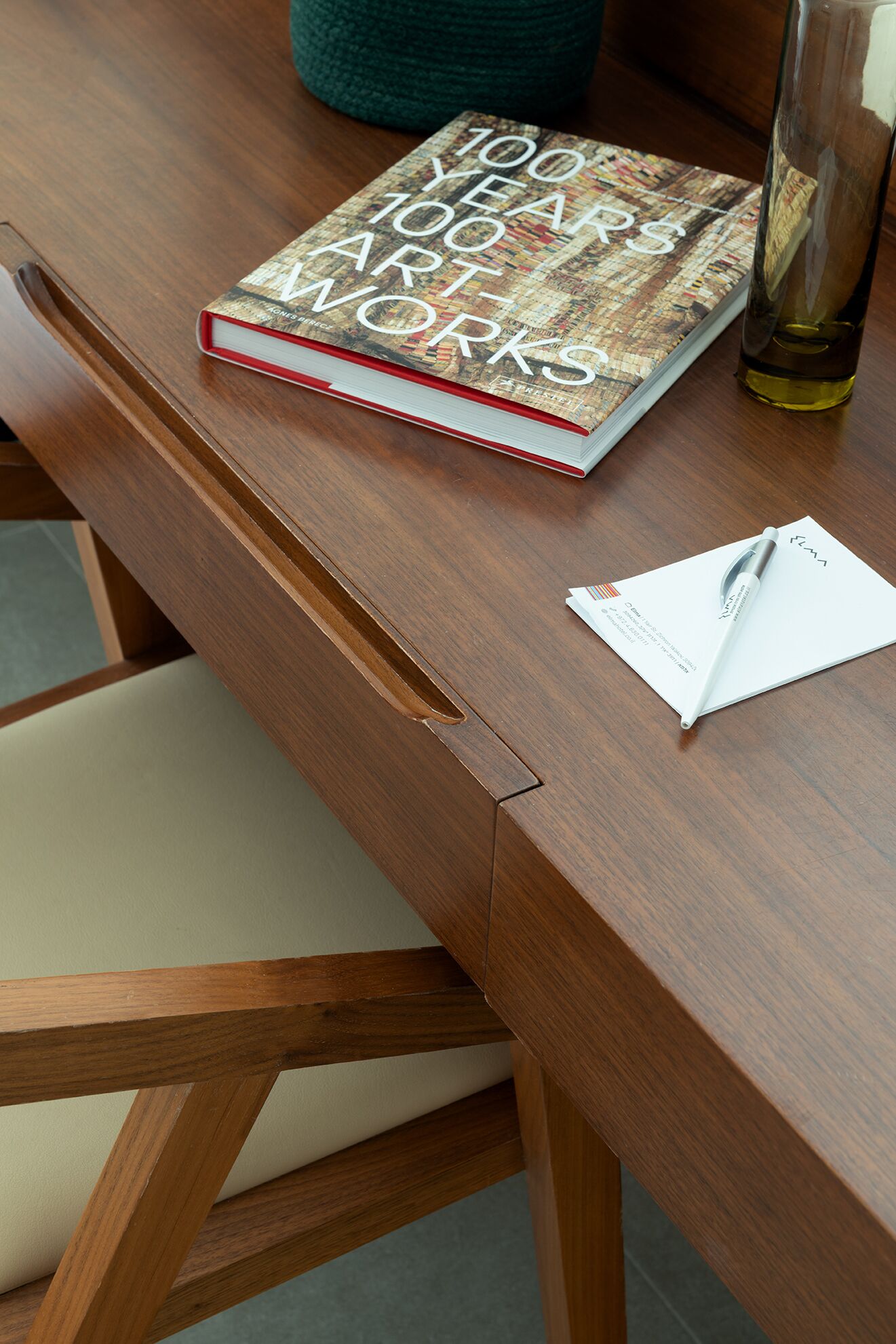 Un libro titulado '100 Años de Obras de Arte' sobre una mesa de madera, con un bolígrafo y papel a un lado.