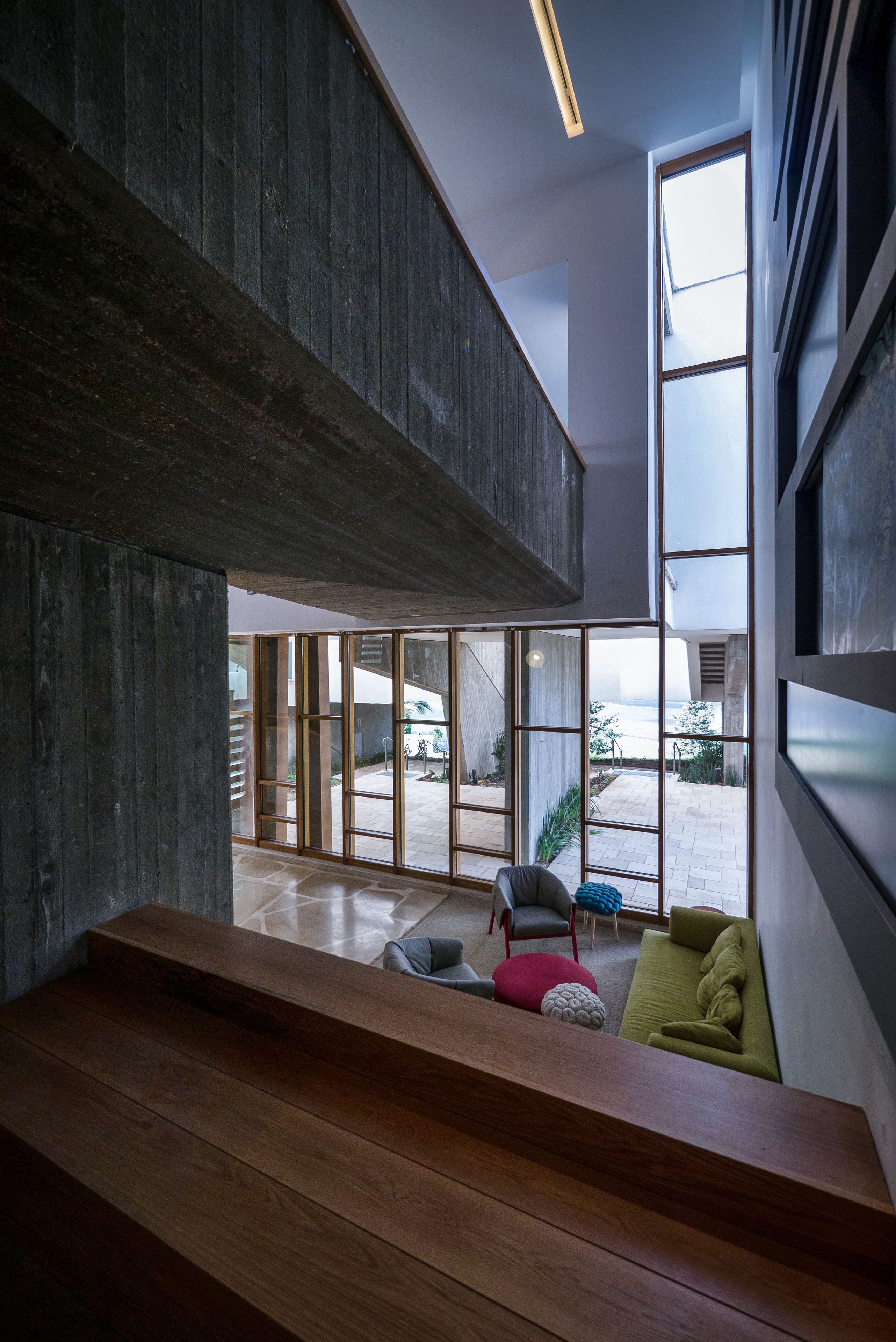 A modern interior with a wooden bench, a green sofa, and a large window offering a view of the outdoors.