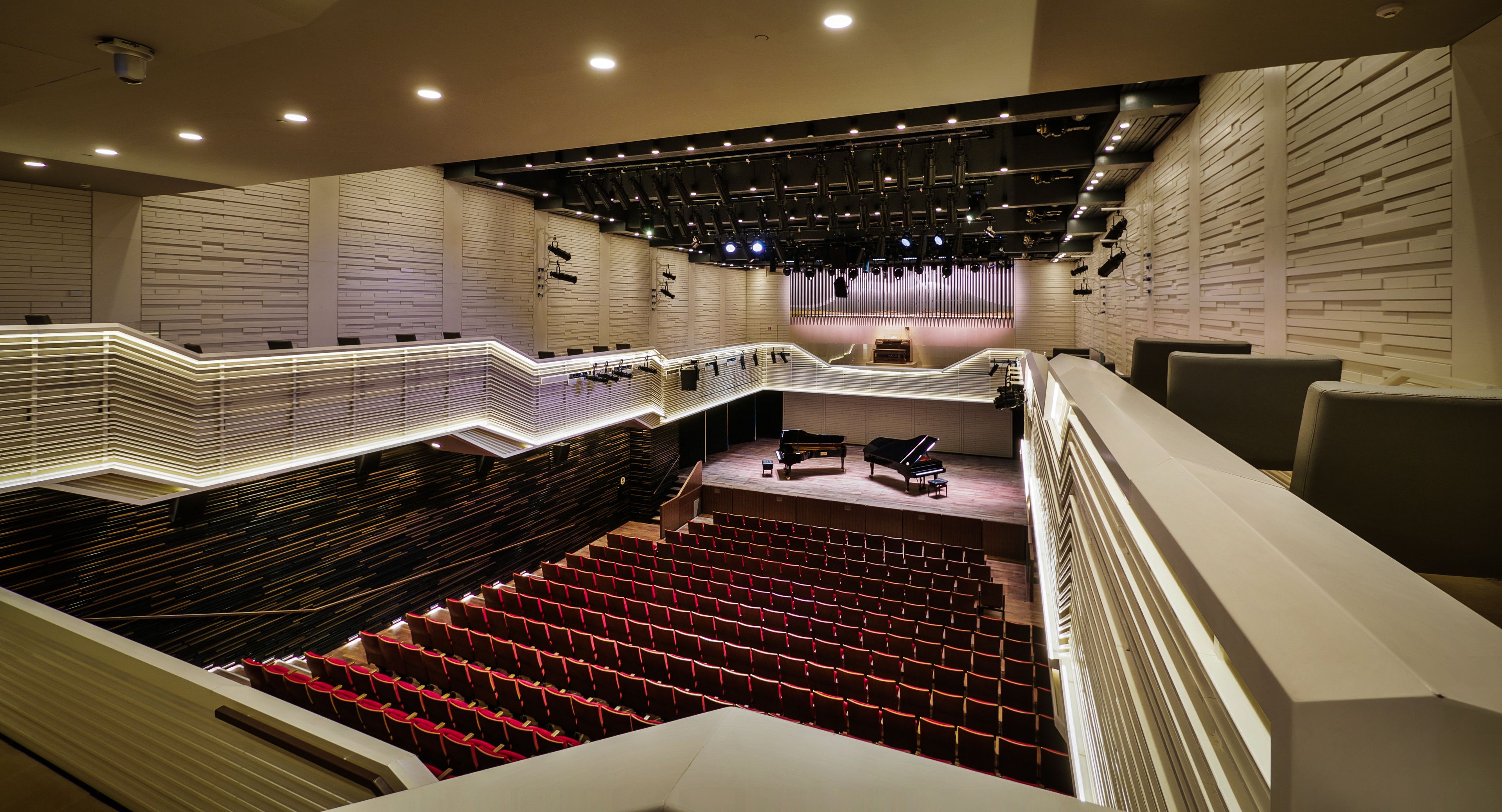 Um teatro com disposição de assentos em níveis, palco com piano e design moderno, com paredes de tijolos aparentes e iluminação embutida.