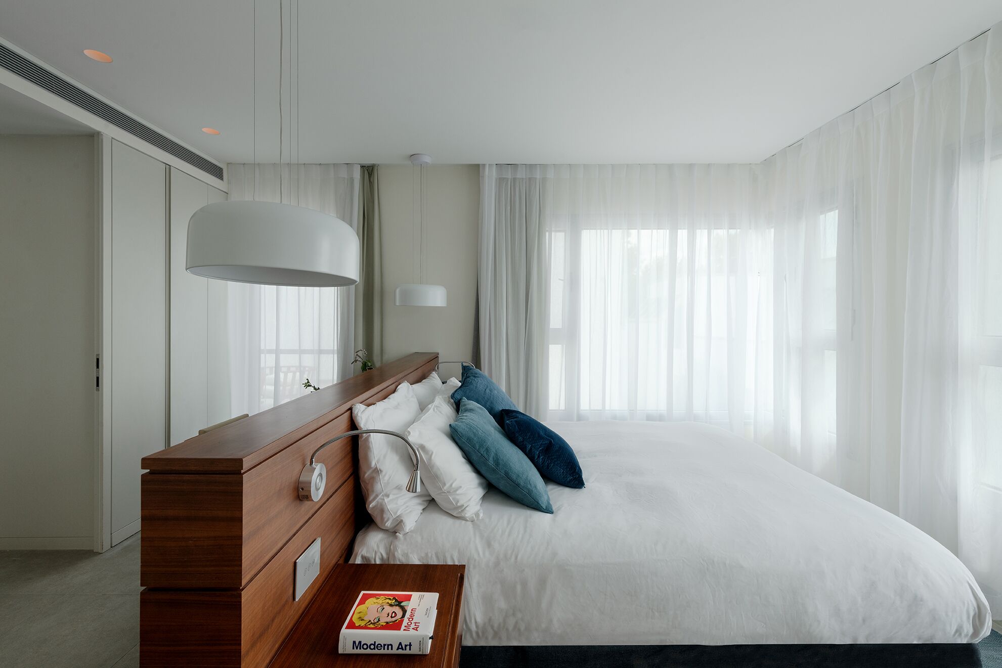 Ein modernes Hotelzimmer mit einem großen Bett, einem hölzernen Schminktisch und einem Nachttisch mit einem Buch.